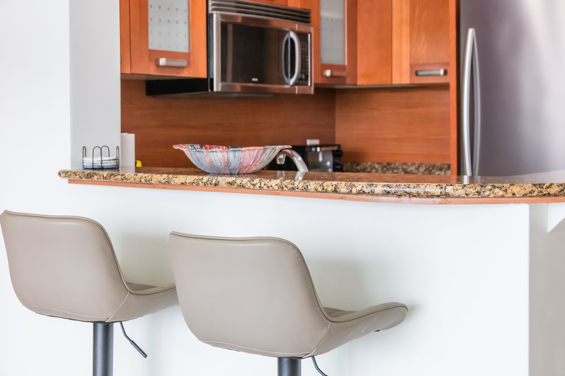 Modern kitchen with granite counter, wooden cabinets, and two beige bar stools