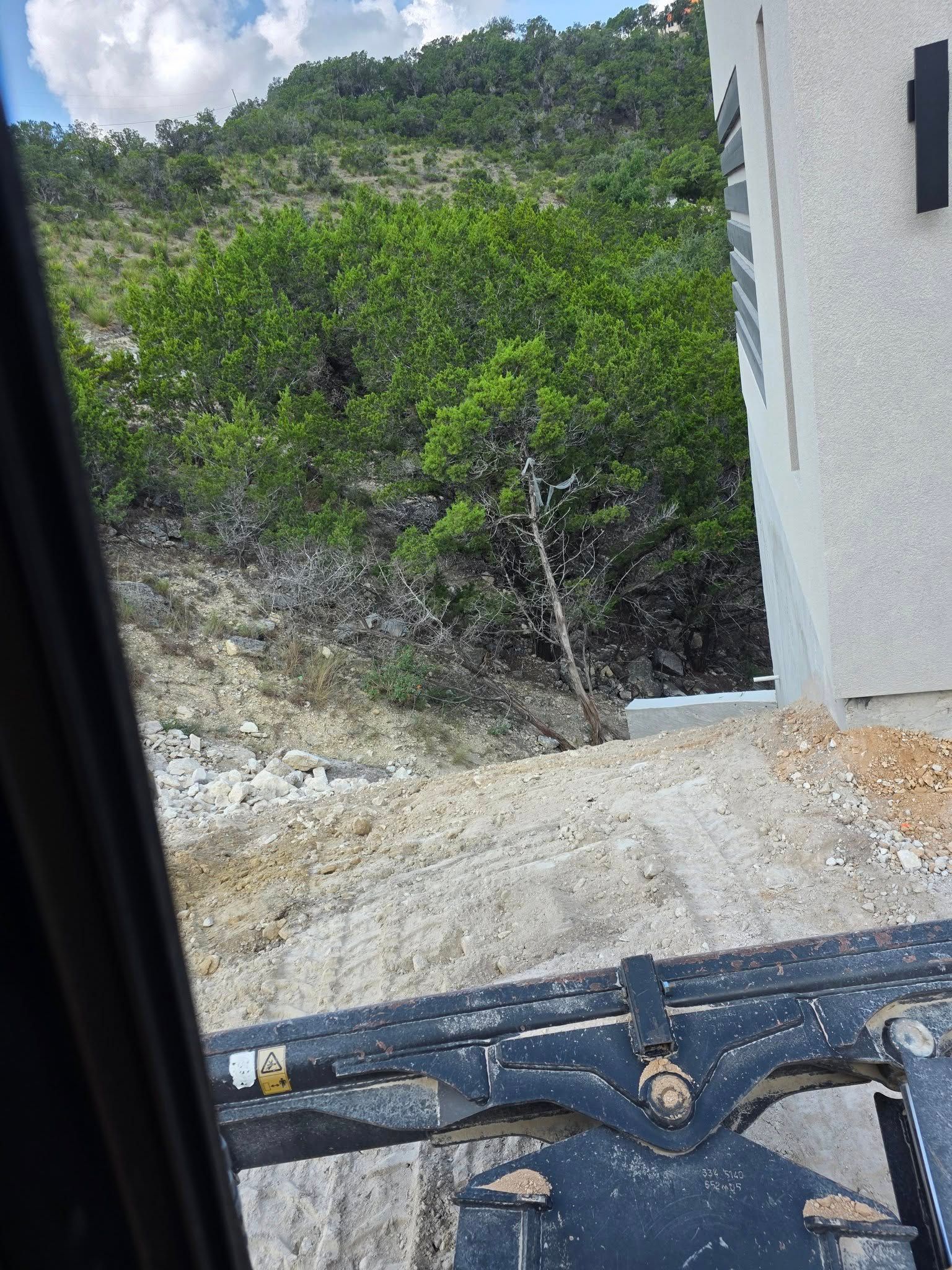 Construction site next to a hillside with green foliage. A building and machinery in view.