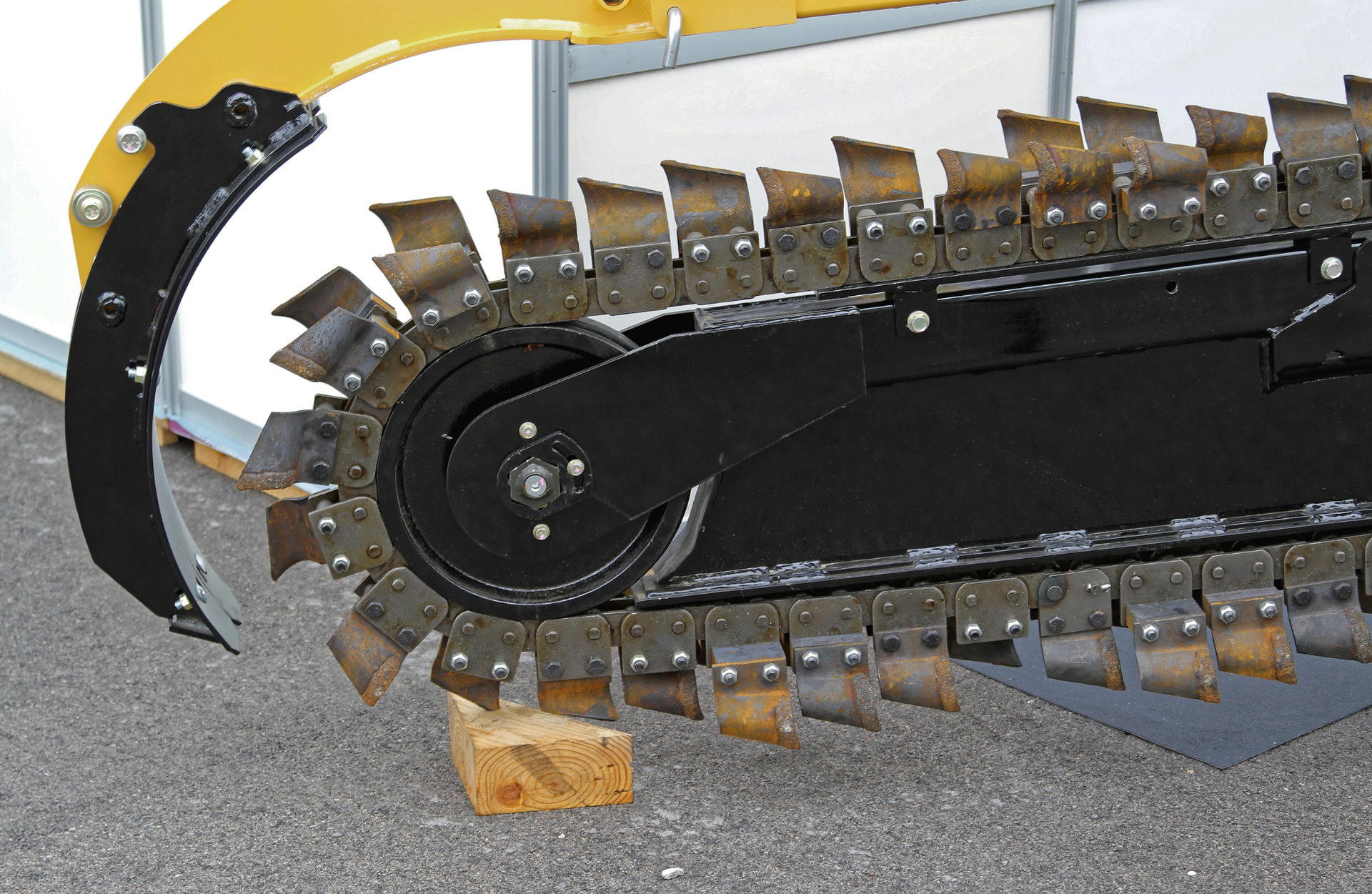 Close-up of a trencher chain with sharp teeth, black metal, angled on a wooden block.