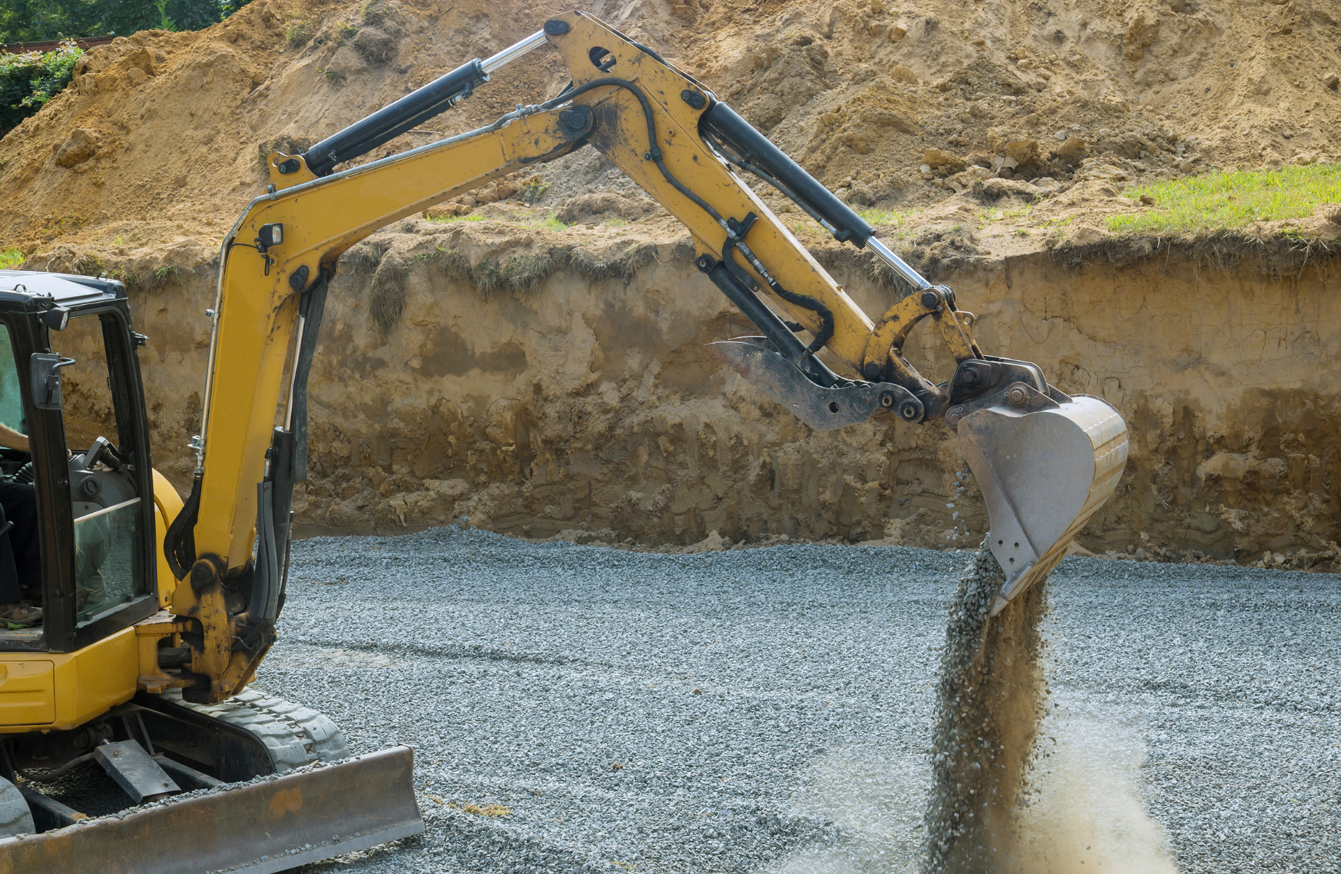 Yellow excavator, digging earth and depositing it onto a gravel surface. Construction site setting.