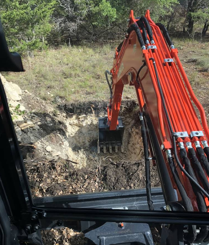 Orange excavator digging into a rocky hillside with a wooded background.