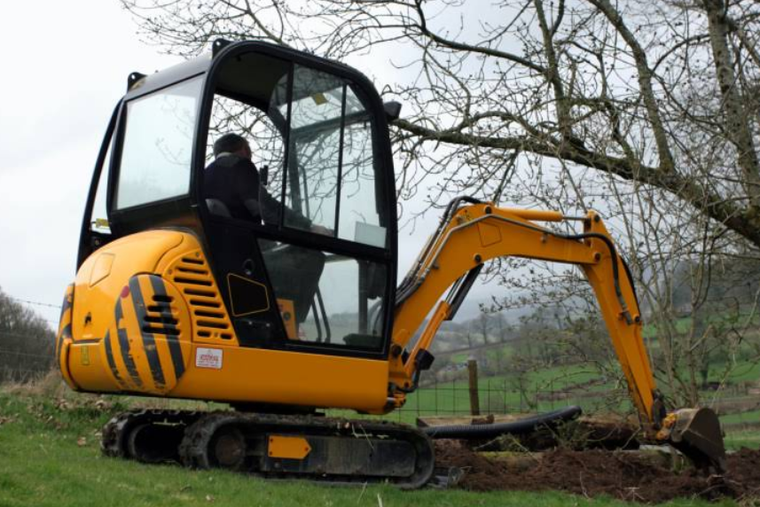 Yellow mini excavator digging dirt in a field with a person operating it.