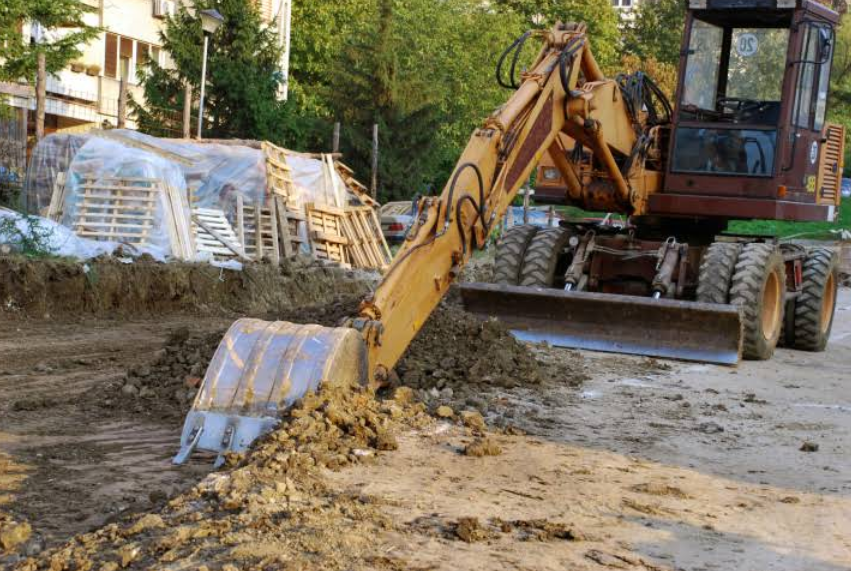 Yellow excavator digging in a dirt area, with pallets in the background.
