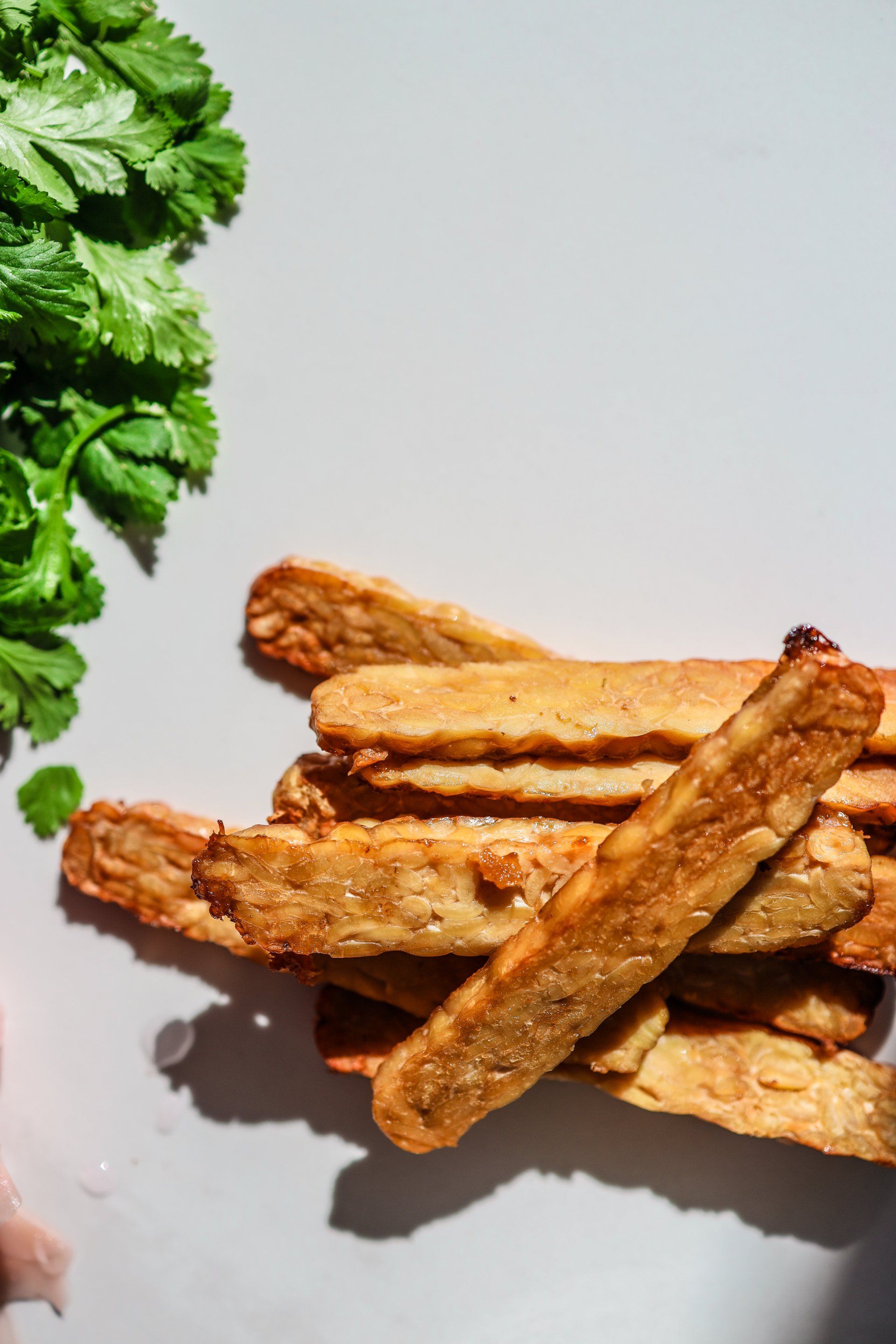 A person is holding a pile of french fries next to a bunch of cilantro.