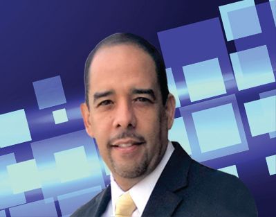 Man in a suit smiles against a blue square background.