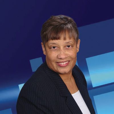 Woman smiling, wearing a pinstripe suit, against a blue, abstract background.