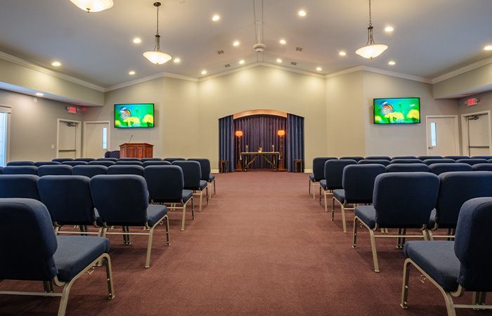 A church with rows of blue chairs and two televisions on the ceiling.