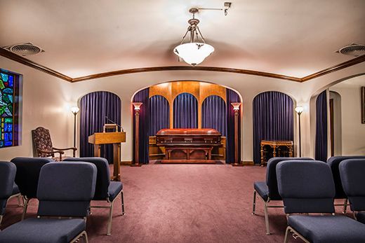 A funeral home with a podium , chairs , a coffin and a stained glass window.