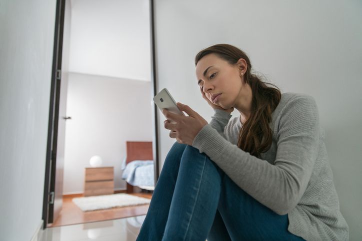 a woman is sitting on the floor looking at her cell phone .