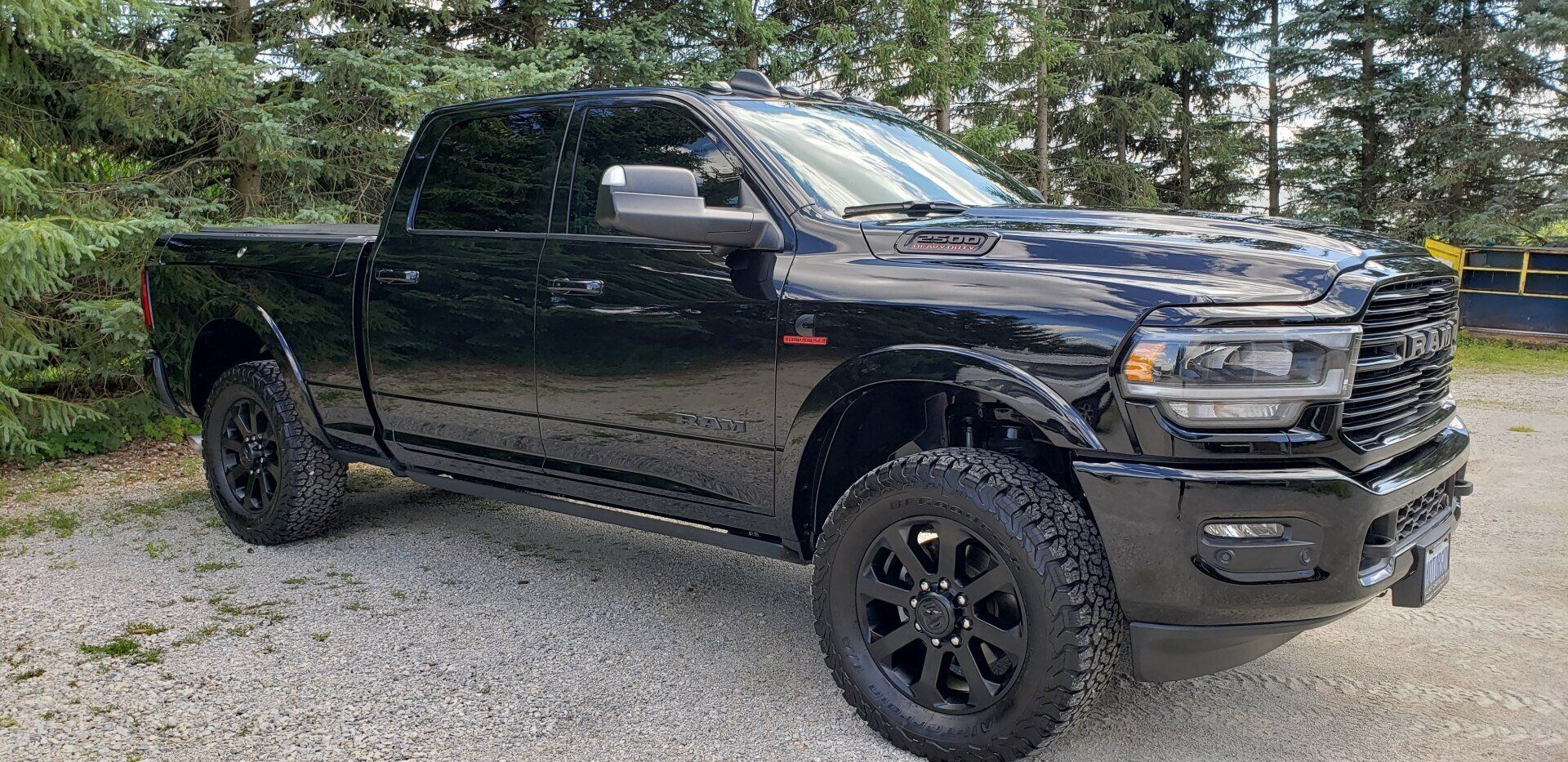 Black pickup truck parked on gravel in front of green trees.