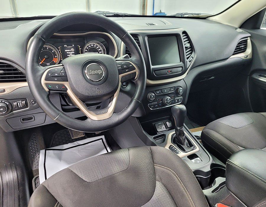 Interior view of a Jeep Cherokee. Dashboard with steering wheel, touchscreen, and console.