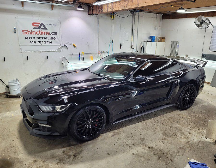 Black Ford Mustang in a garage; auto detailing shop logo visible.
