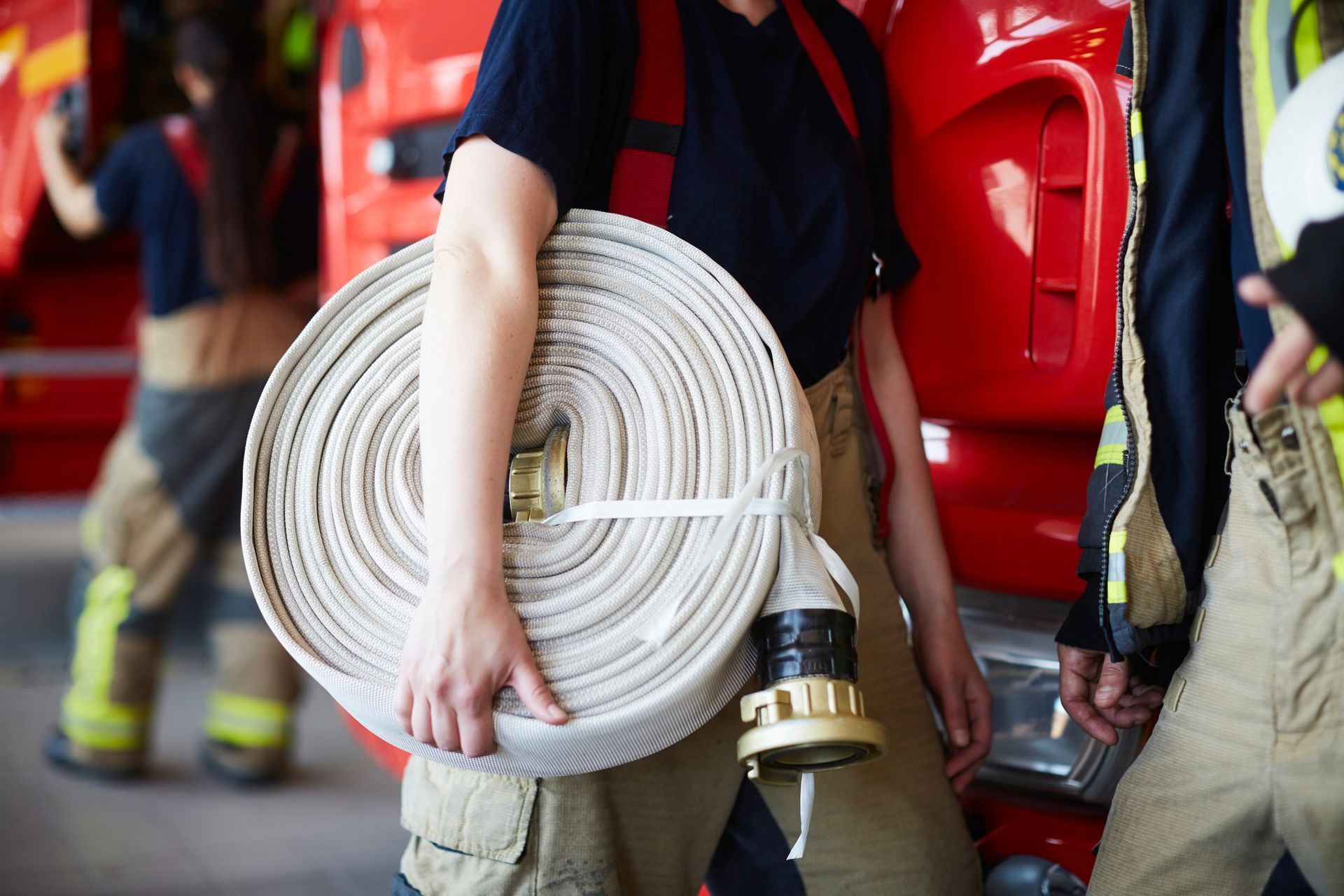 A woman is holding a fire hose in front of a fire truck.
