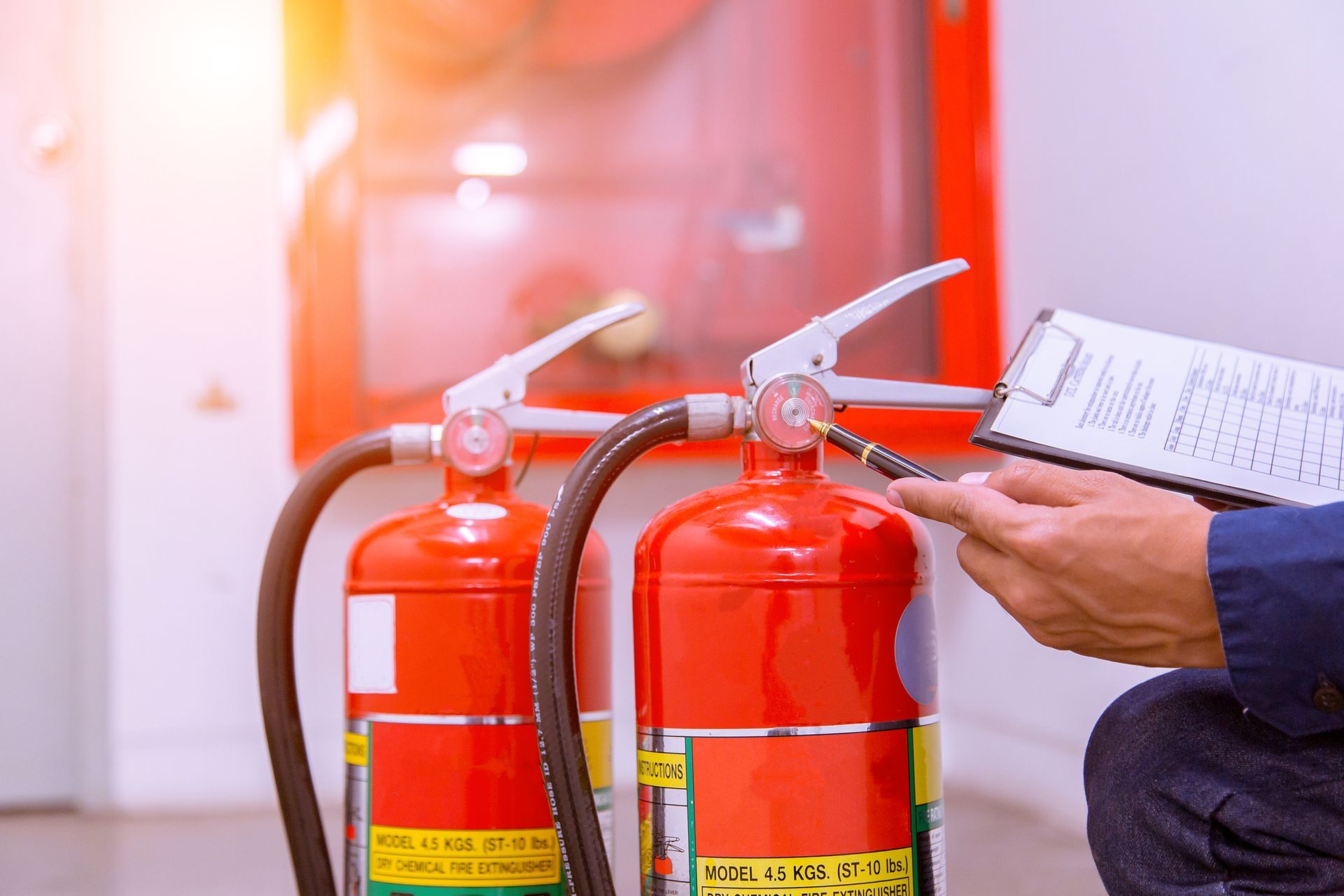A man is sitting next to two fire extinguishers and holding a clipboard.