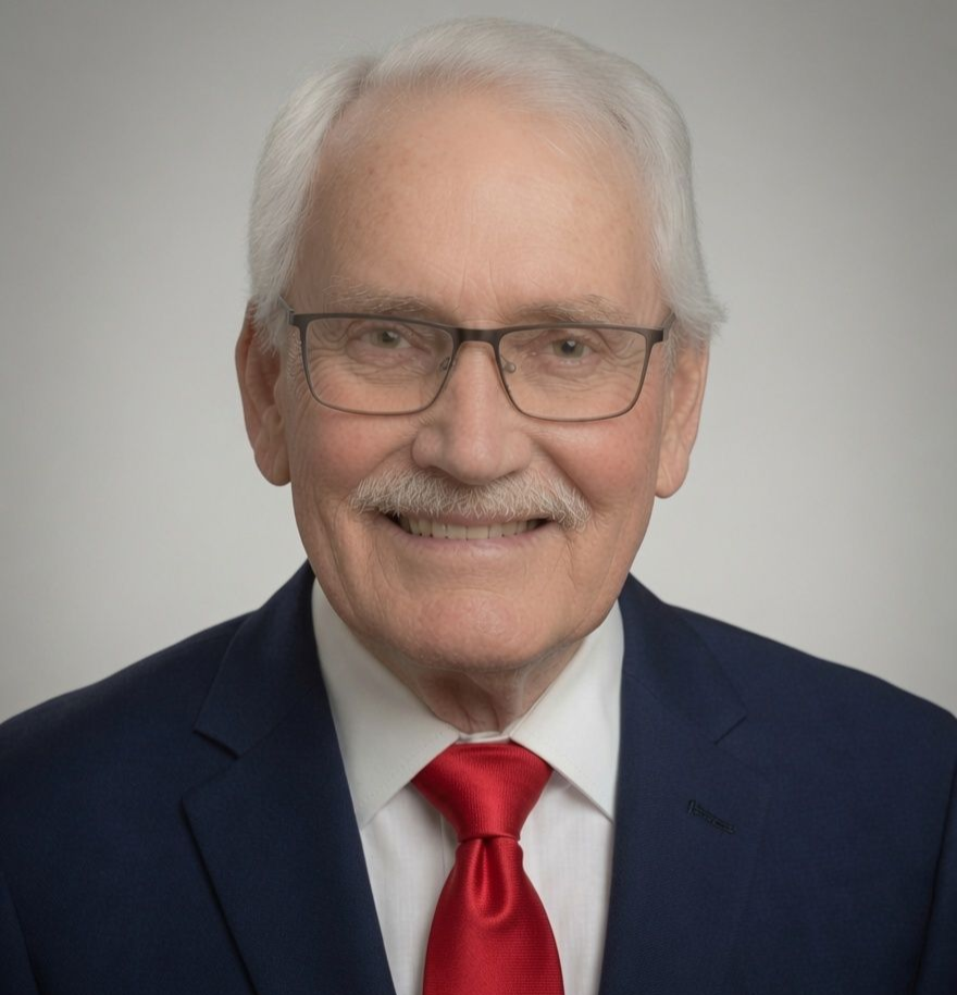 Portrait of a smiling man in a navy suit, white shirt, and red tie against a gray background