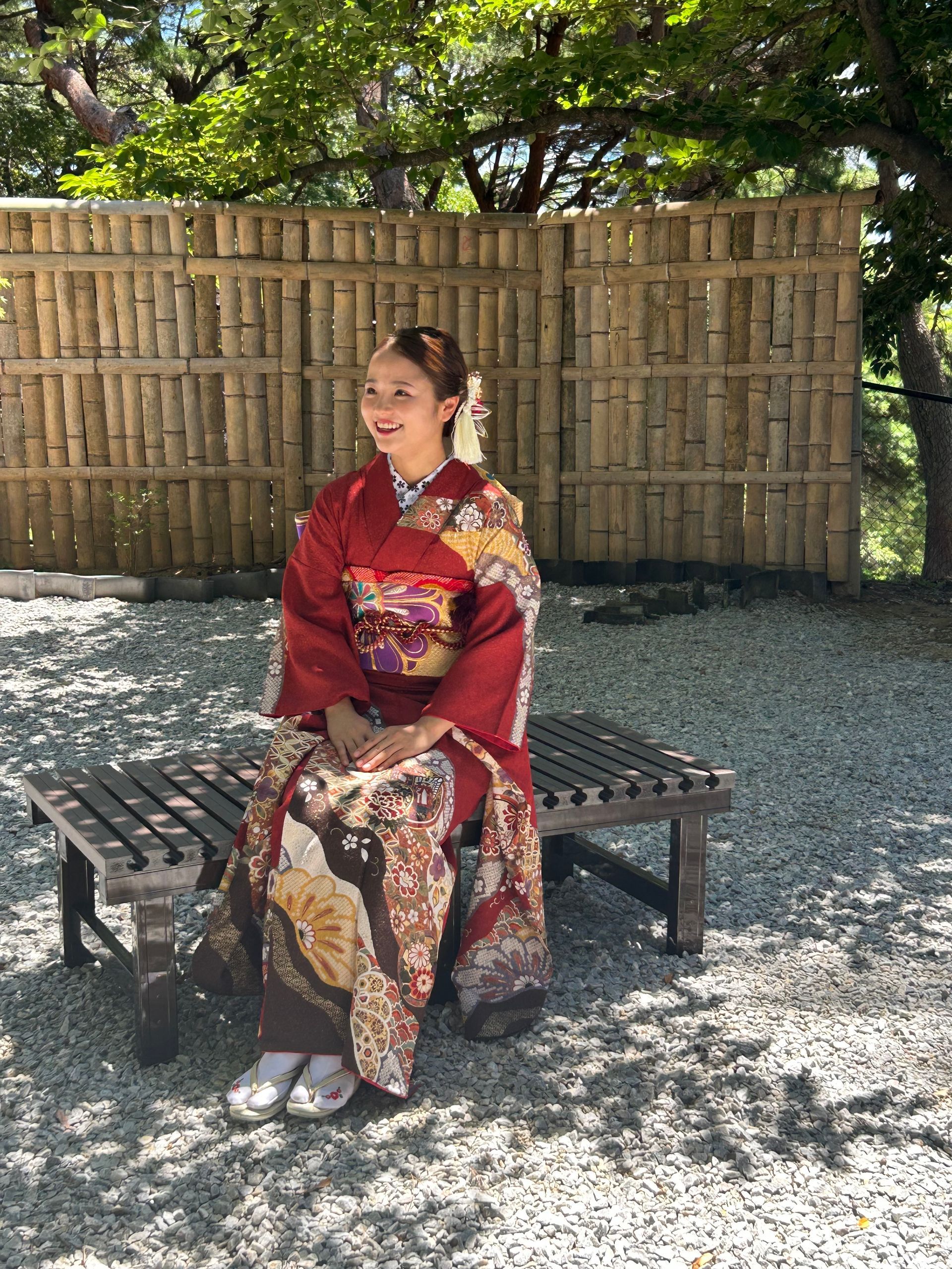 A woman in a red kimono is sitting on a bench.