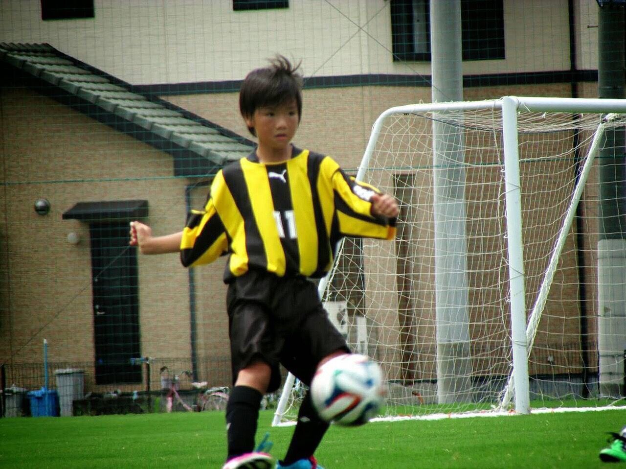 A young boy in a yellow and black striped shirt is kicking a soccer ball