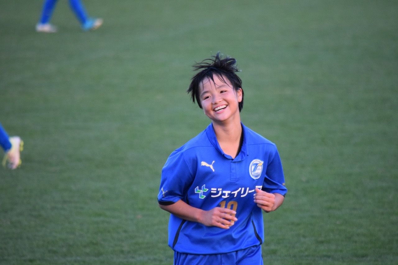 A young boy in a blue soccer jersey is smiling on a field.