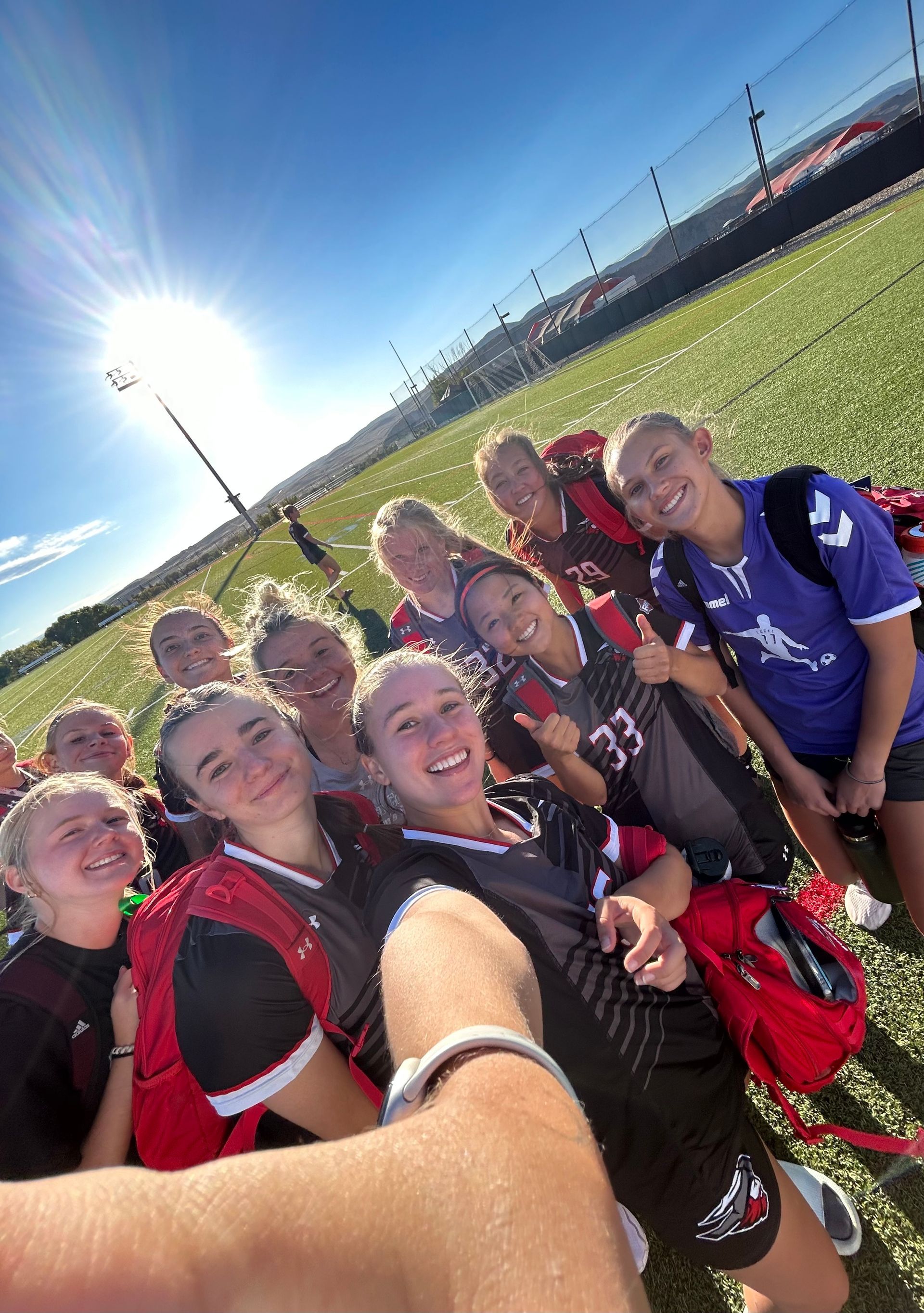 A group of young girls are taking a selfie on a soccer field.