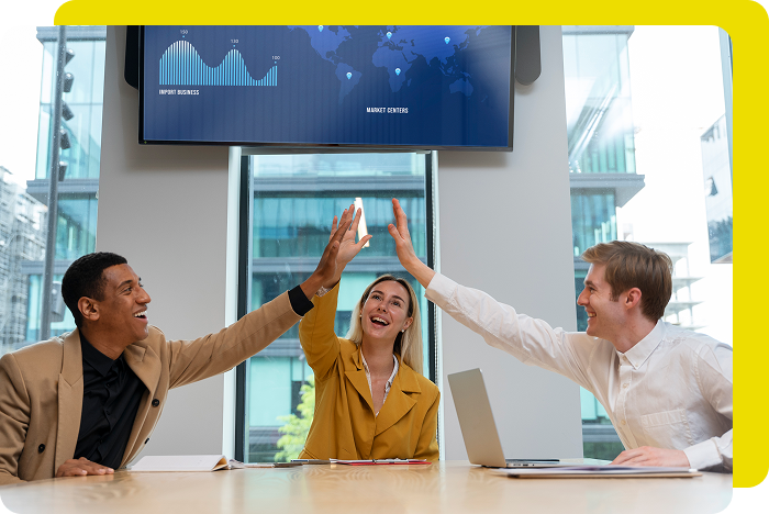 Three people high-fiving in a modern office, with a screen displaying data charts.