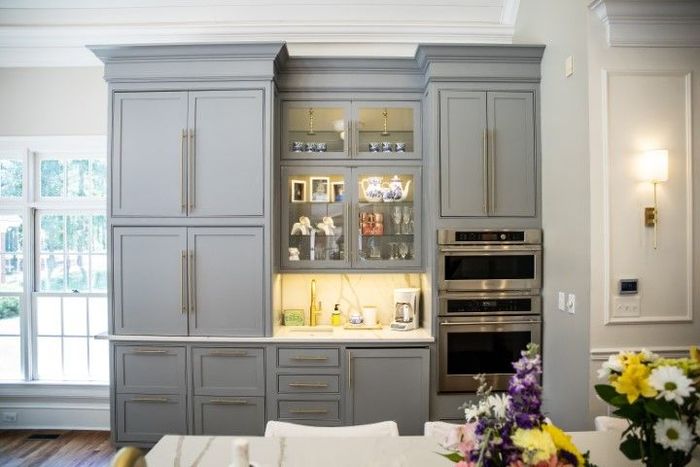 Gray kitchen cabinets with built-in appliances and a glass-front display case, set against a light-colored wall.