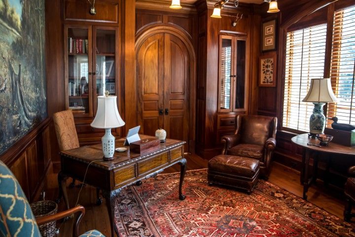 Cozy wooden study with desk, armchair, bookcase, and Persian rug. Warm lighting and ornate details.