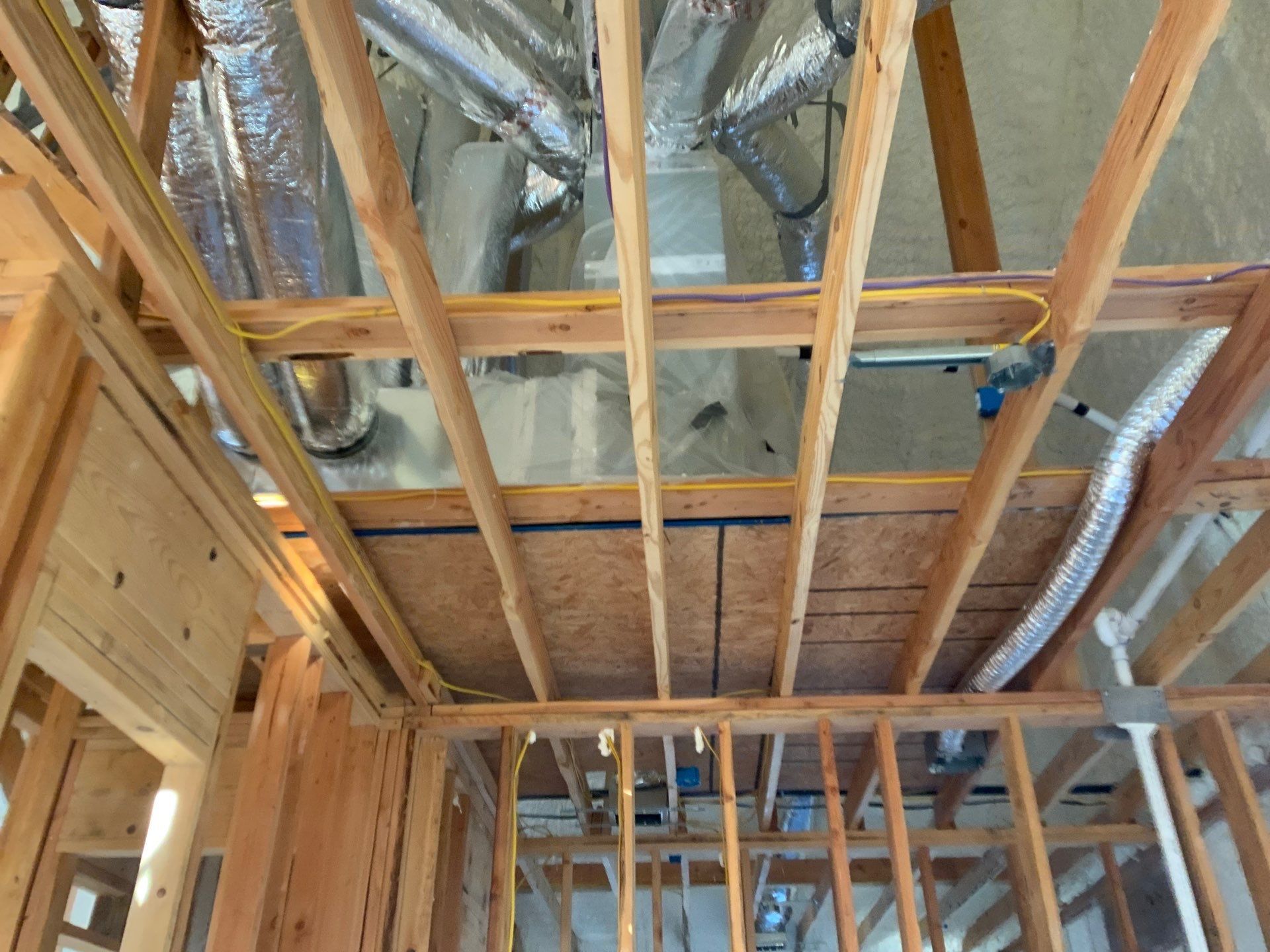 The ceiling of a house is being built and has a lot of pipes coming out of it.