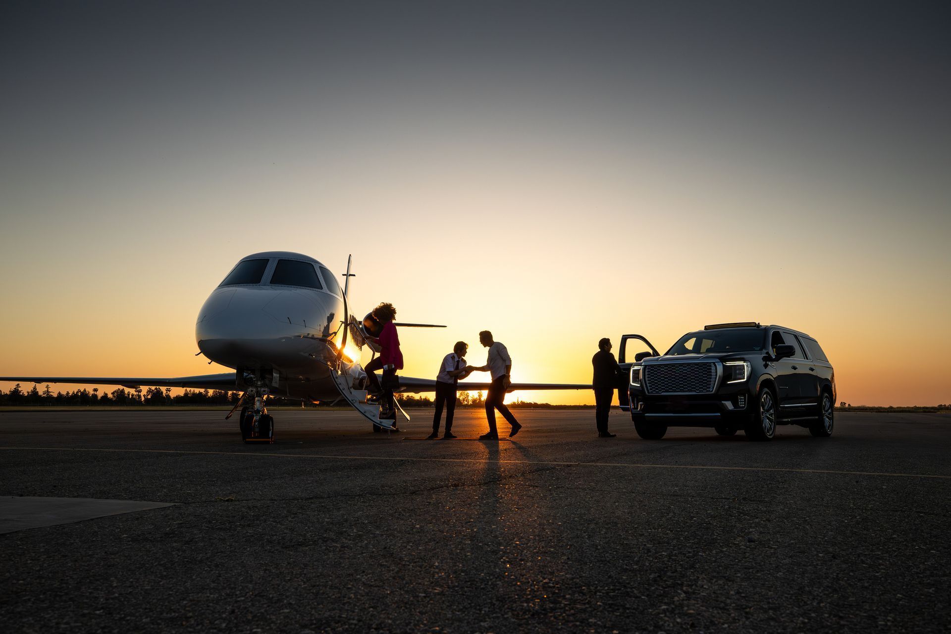 Airplane on tarmac, people boarding, SUV parked, sunset.