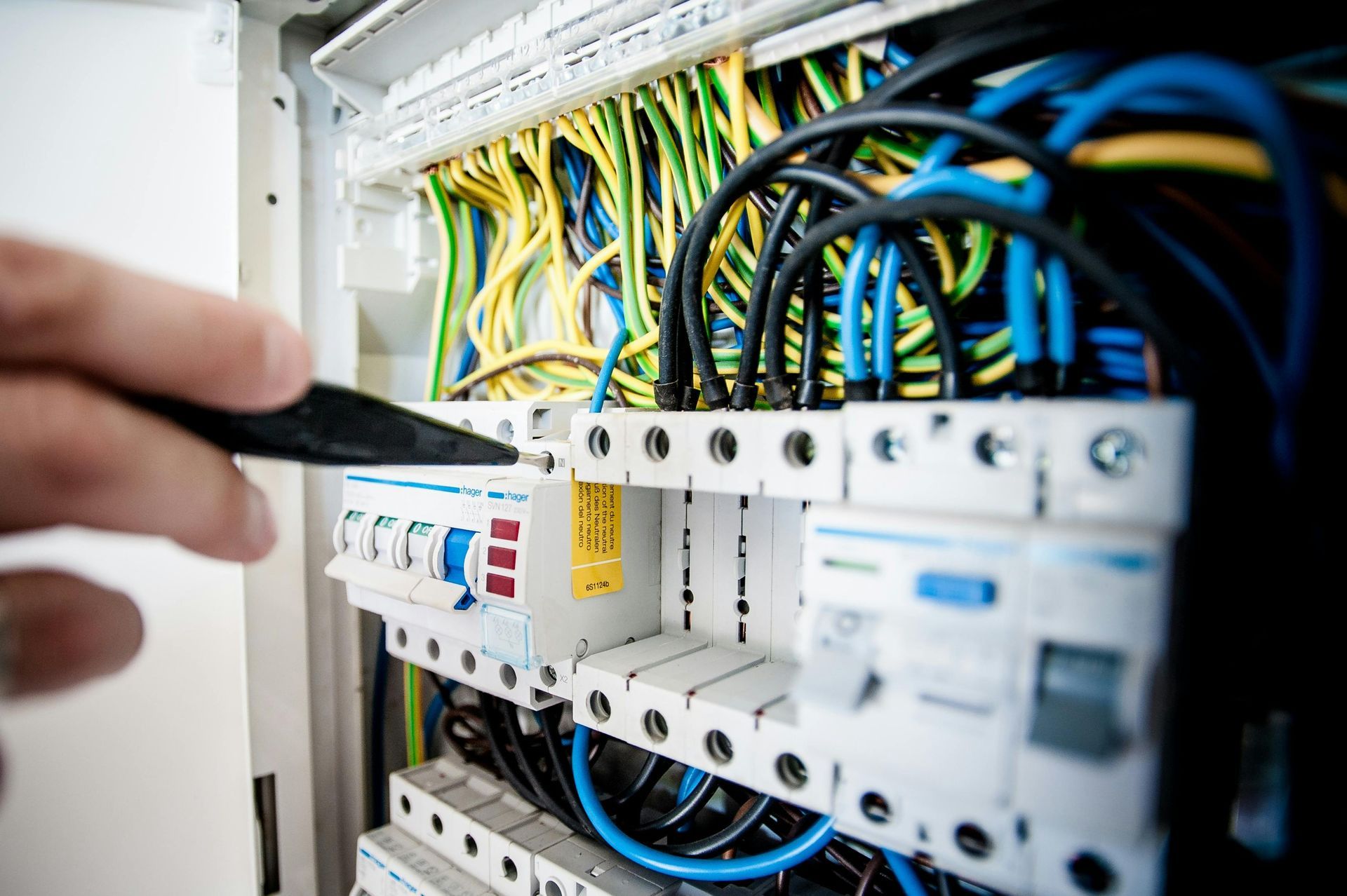 Close-up of an electrician working on a fuse box, with colorful wires and tools.