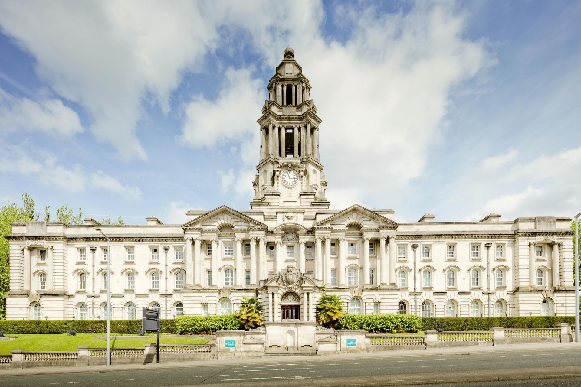 Large, ornate, light-colored building with a tall clock tower under a partly cloudy sky.