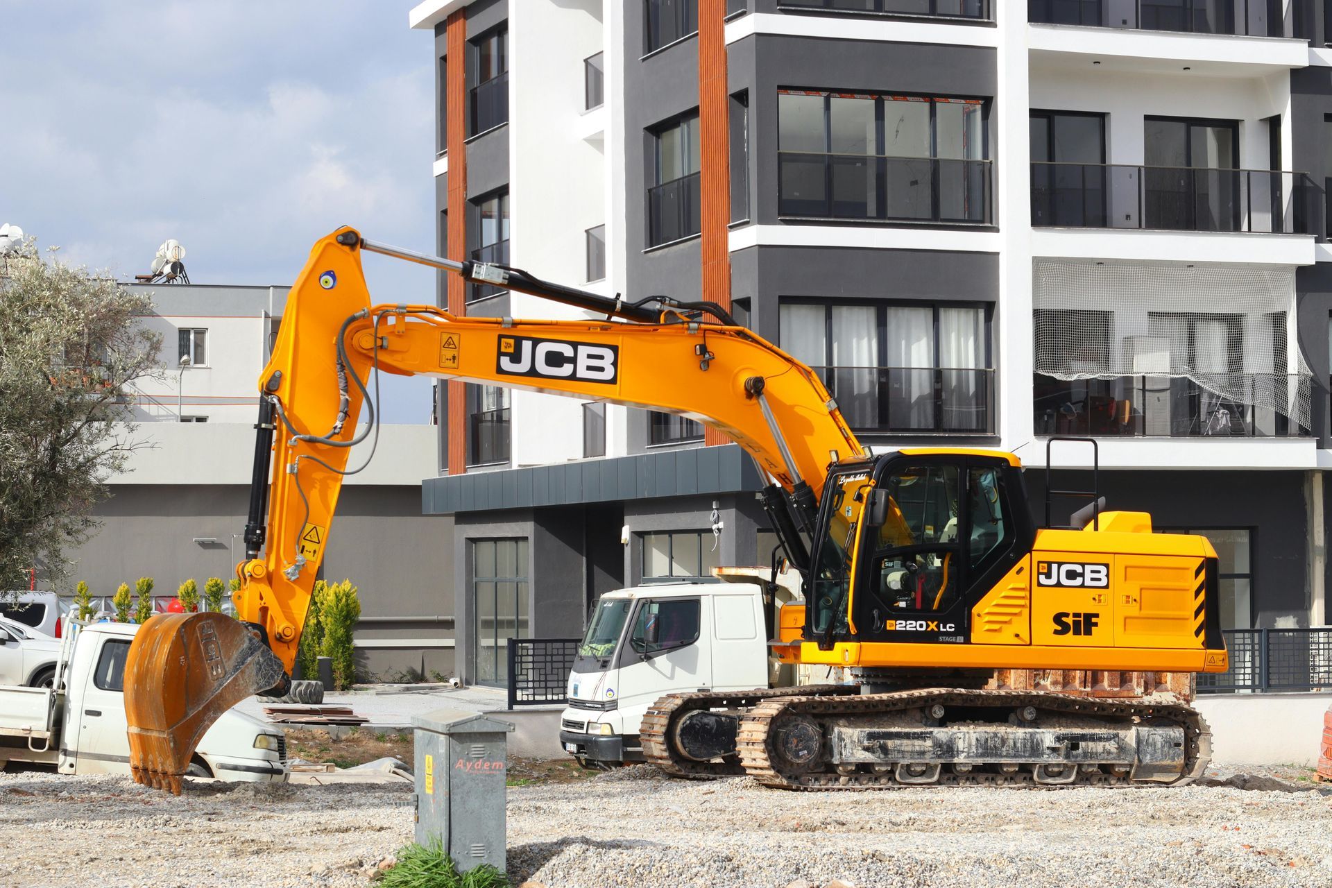 Yellow JCB excavator digging at a construction site near an apartment building.