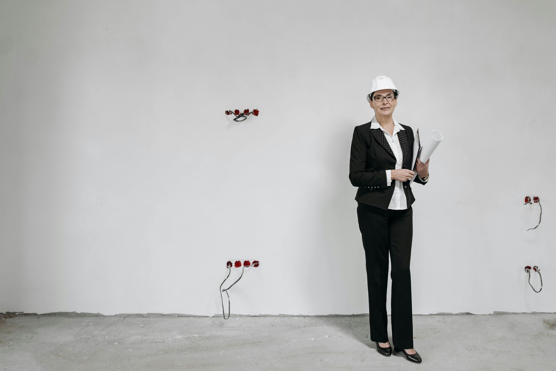 Woman construction worker in a white hard hat and suit, holding blueprints, stands in an unfinished room.