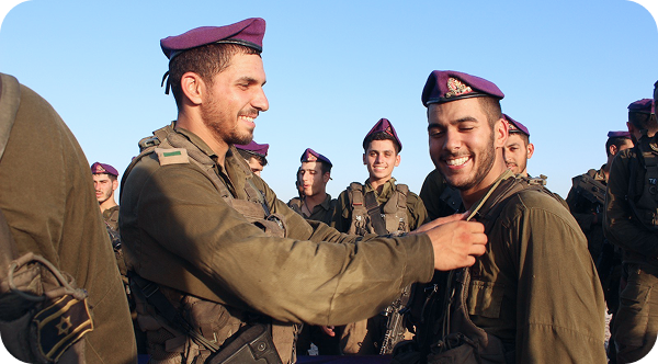A group of soldiers are standing together and one of them is putting a medal on another soldier 's chest.