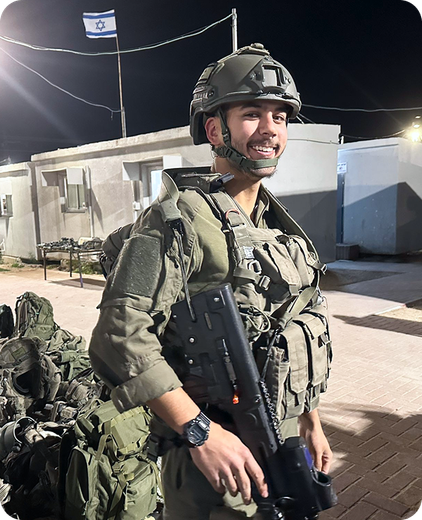 A soldier is standing in front of a building with a flag in the background.