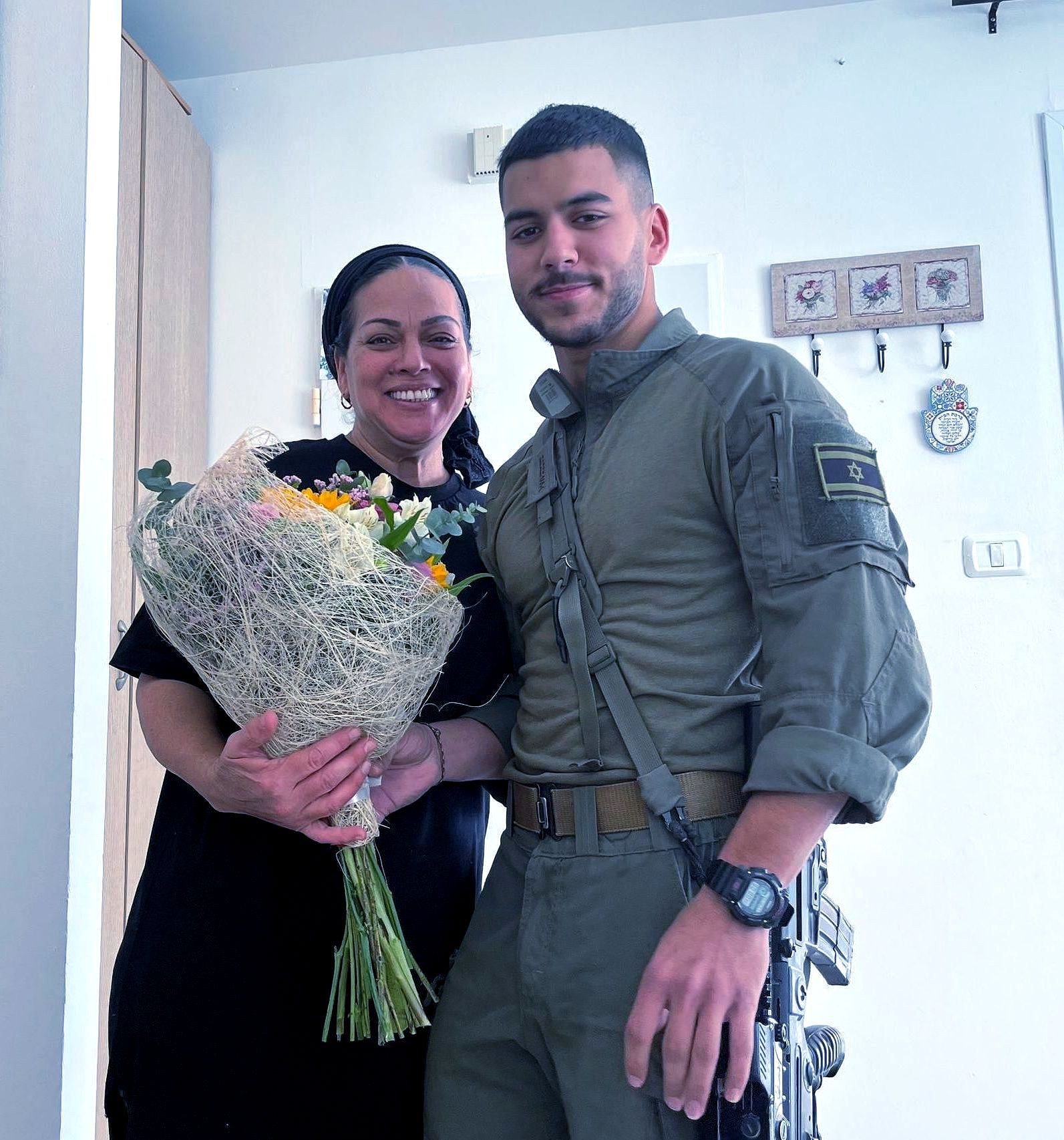 A man in a military uniform stands next to a woman holding a bouquet of flowers