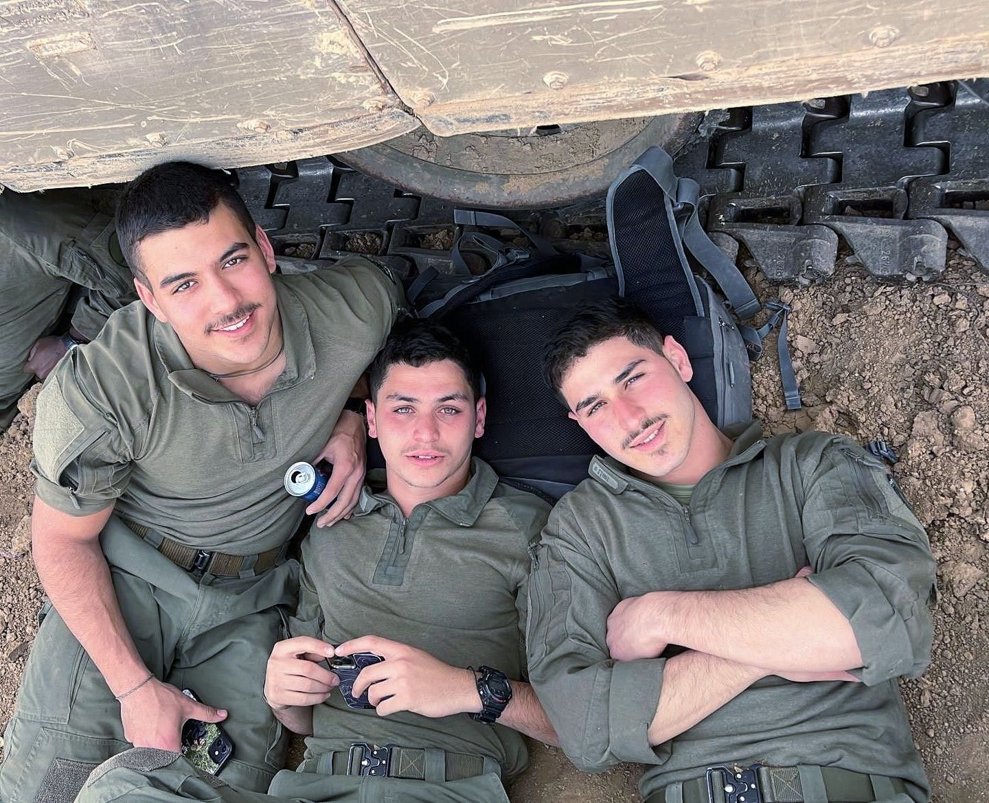 Three soldiers are laying on the ground under a vehicle.