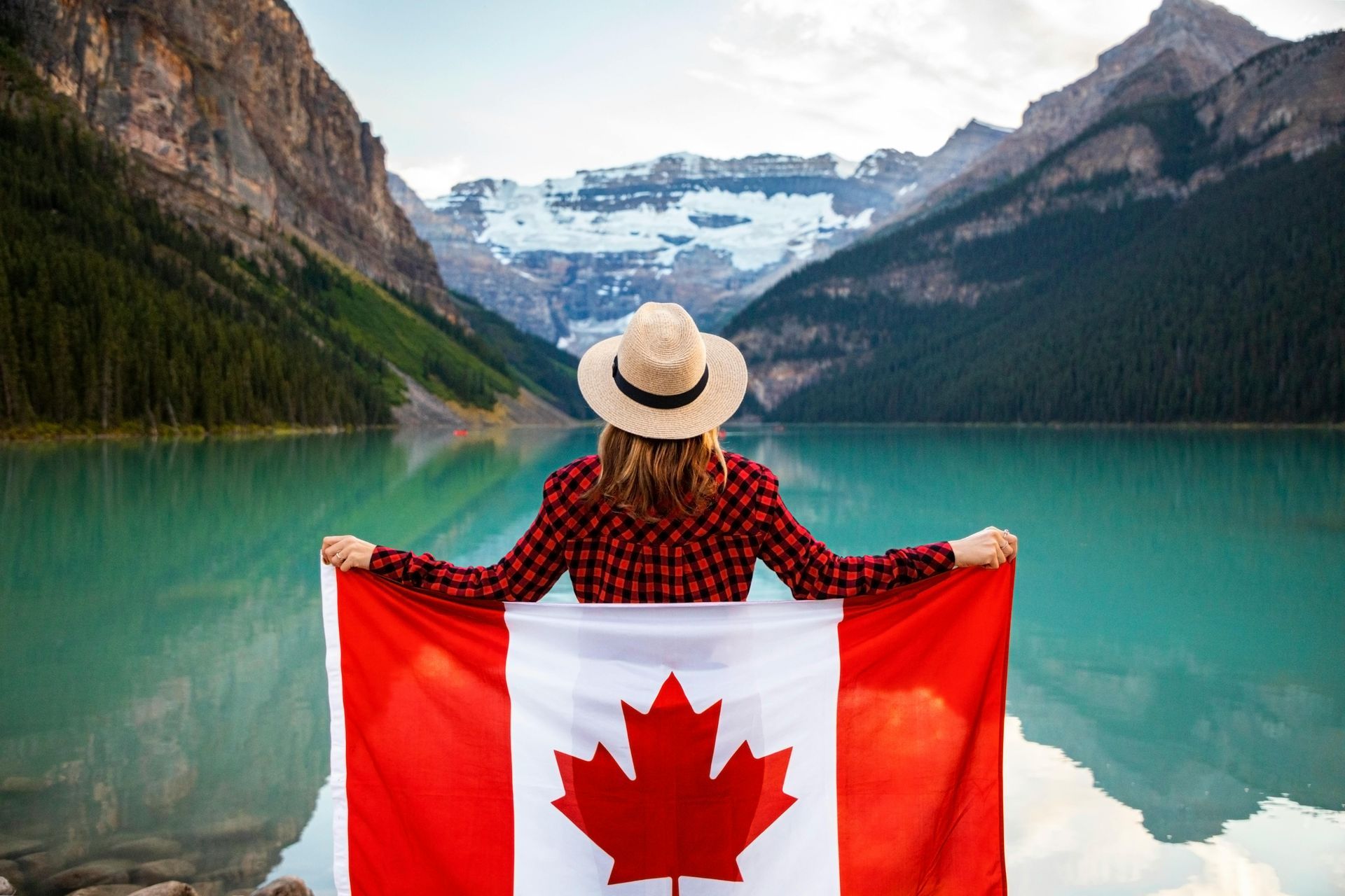 A woman standing infront of a lake with the Canadian flag held behind her. 