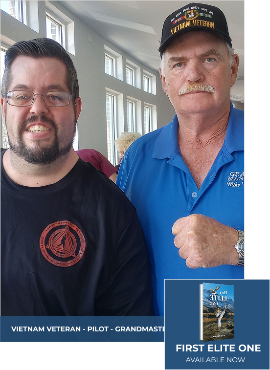 Two men smiling, one in a Vietnam Veteran hat, blue shirt, fist up; the other in a black shirt, glasses.