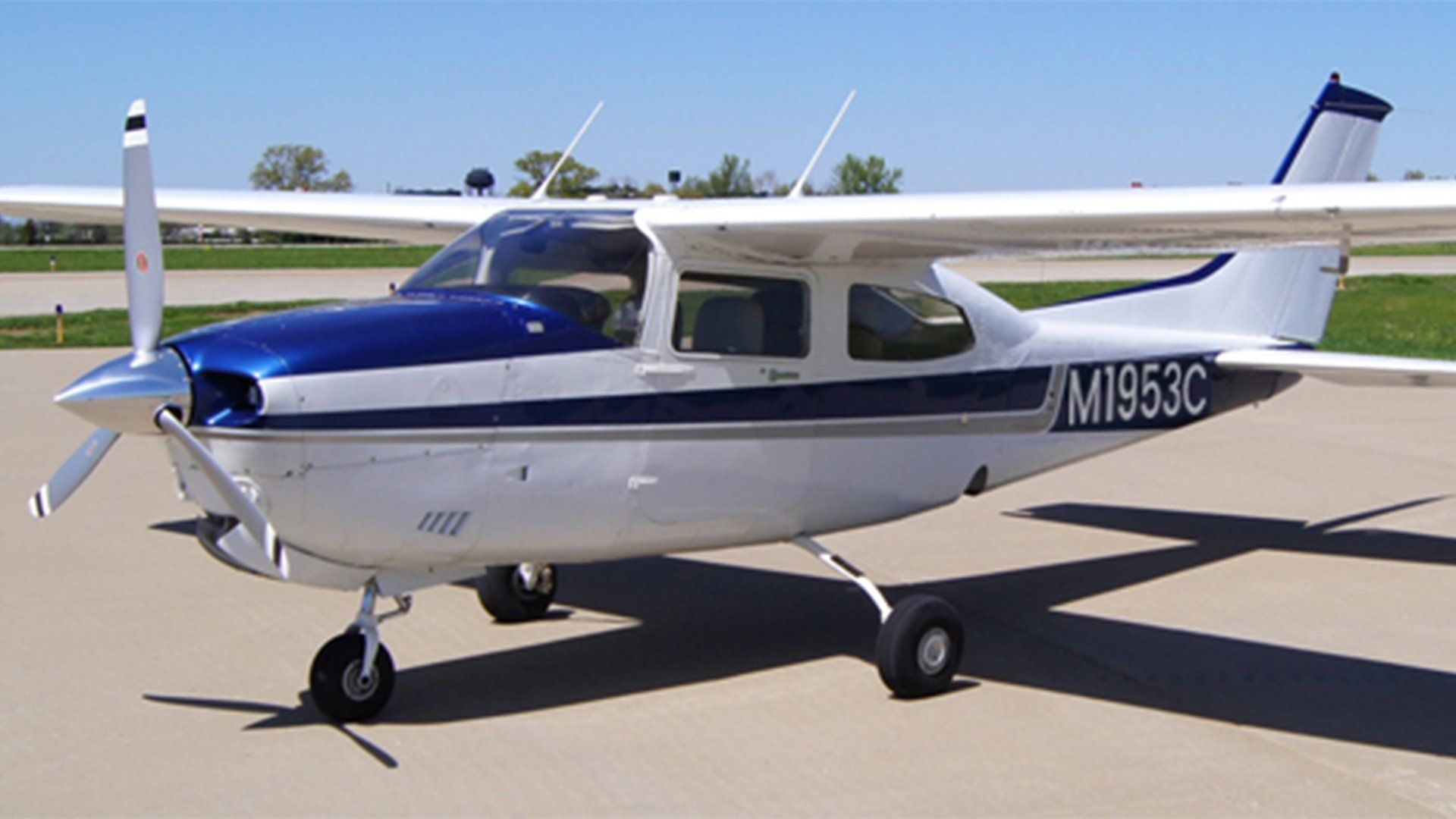 Blue and white single-engine Cessna aircraft on a paved runway. The plane is facing left.