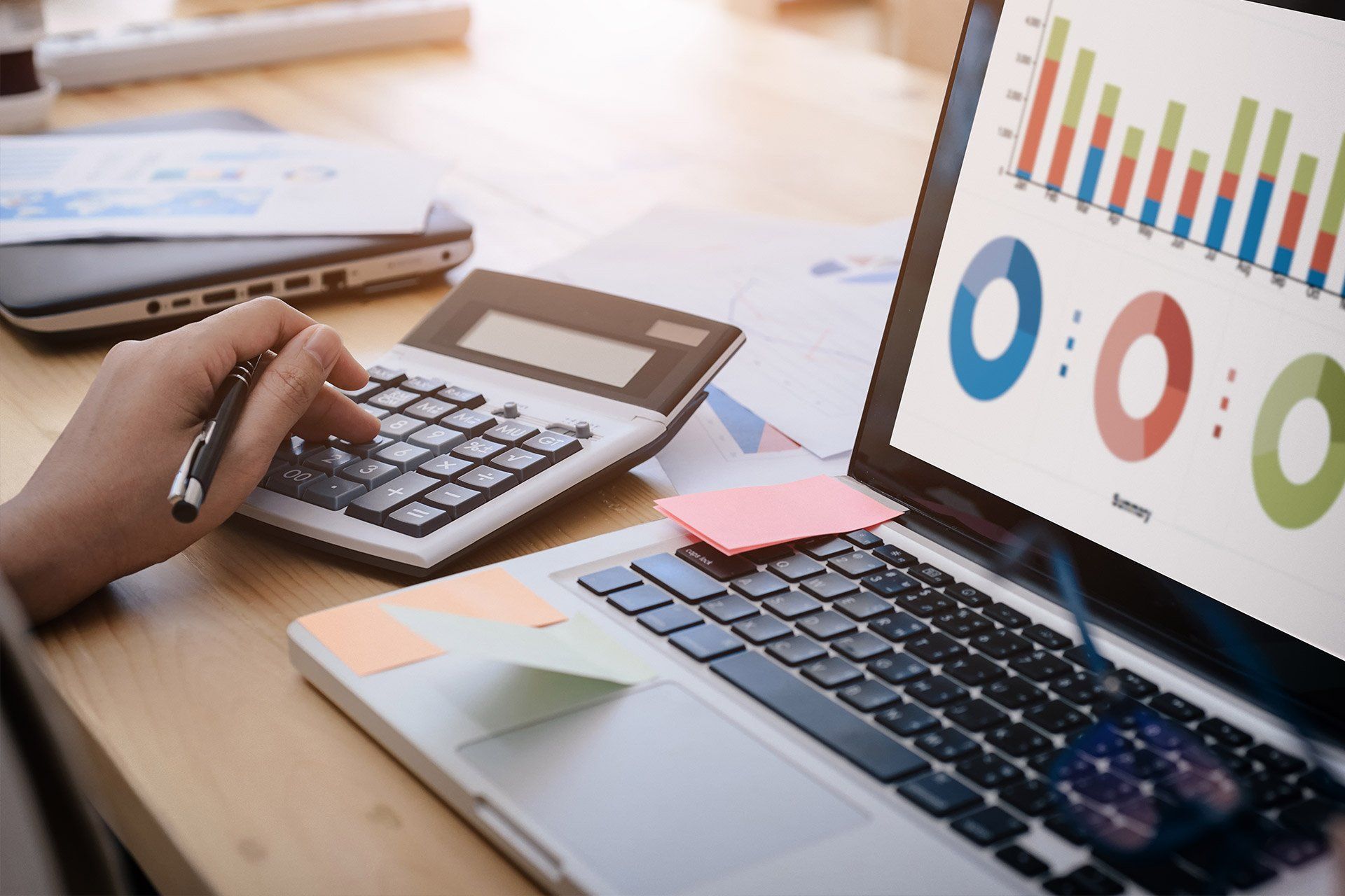 Persona calculando con calculadora, portátil mostrando gráficos, análisis financiero.
