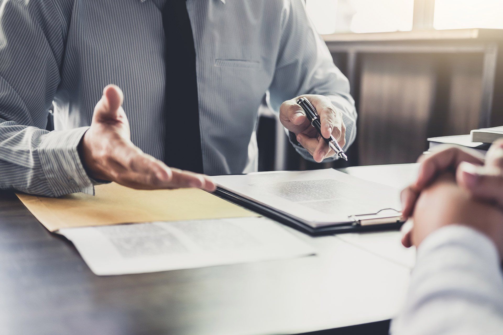 Un hombre de traje hace gestos hacia otra persona sentada en un escritorio para entregarle unos documentos.
