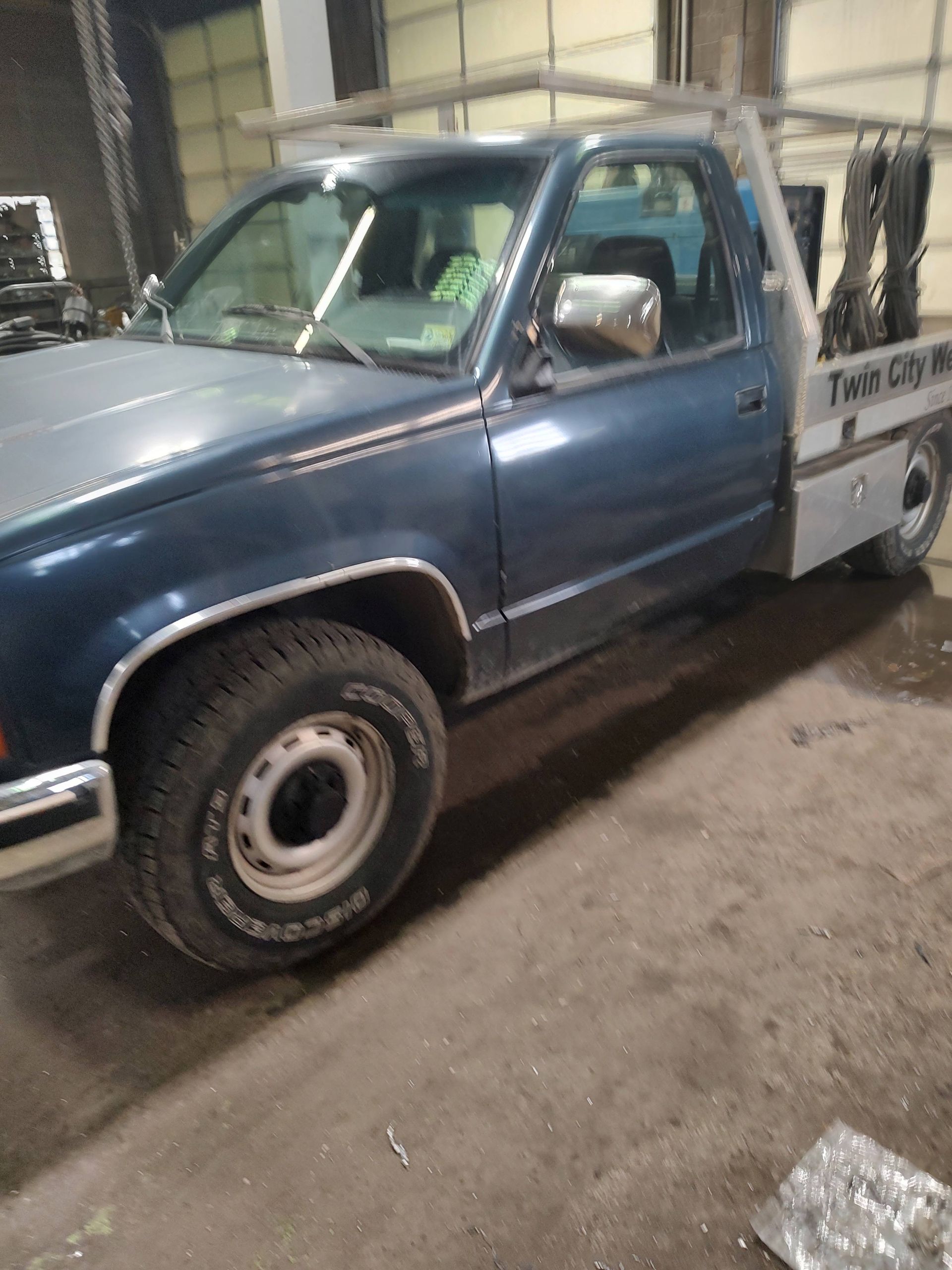 A blue truck is parked in a garage next to a garage door.