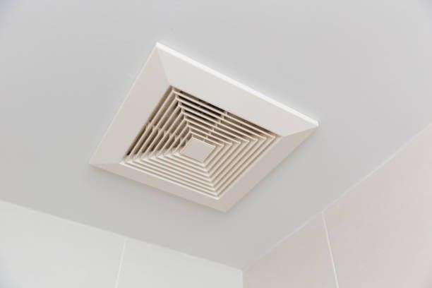 A square ventilation fan is hanging from the ceiling of a bathroom.
