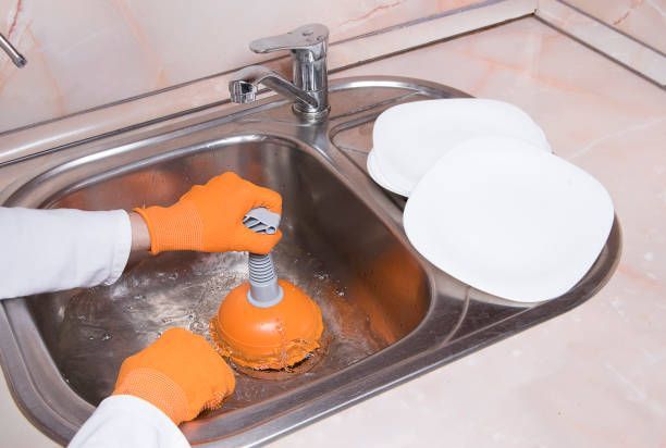 A person is using a plunger to clean a kitchen sink.