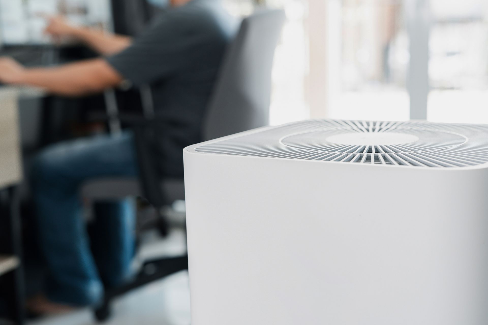 A man is sitting at a desk in front of an air purifier.
