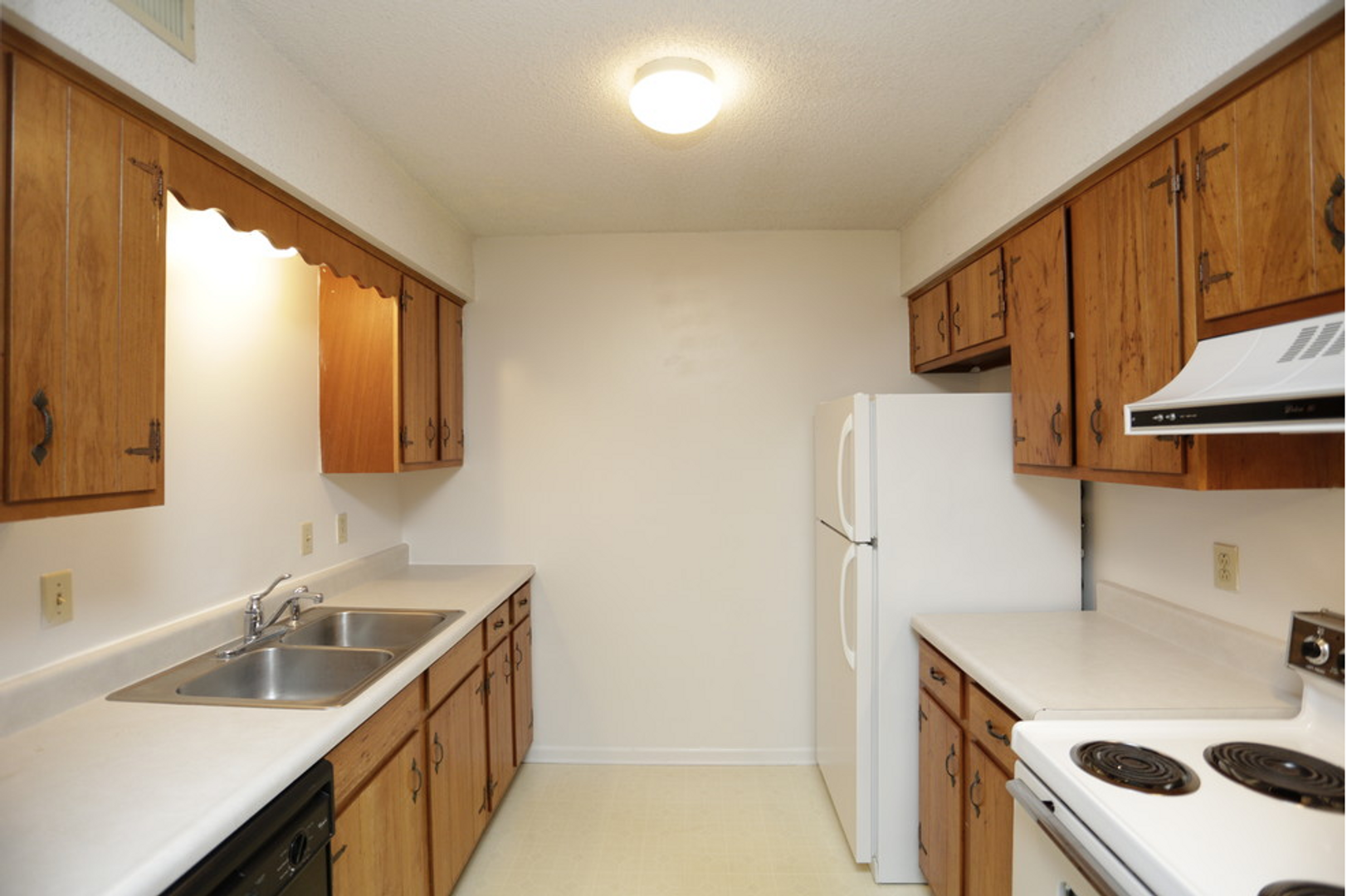 An empty kitchen with wooden cabinets and a white refrigerator