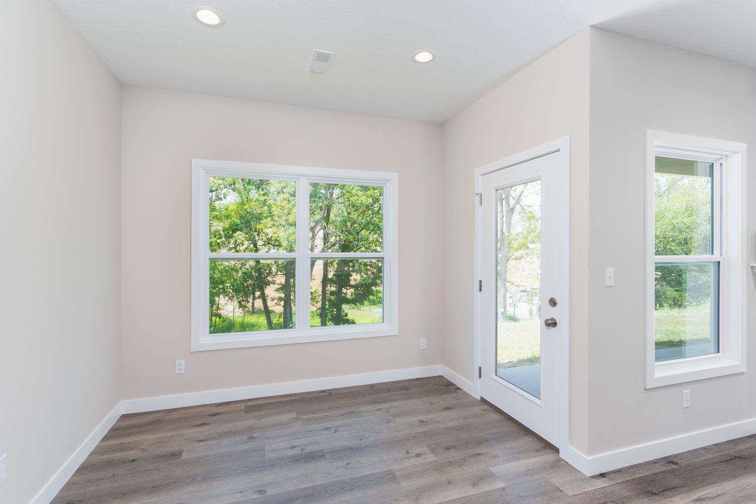 An empty room with hardwood floors , two windows and a door.