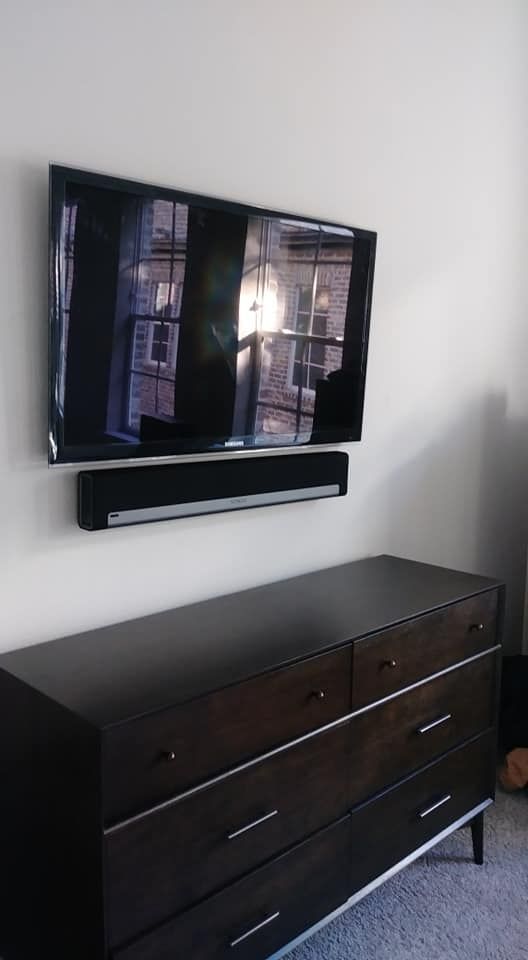A flat screen tv is mounted on a wall above a dresser.