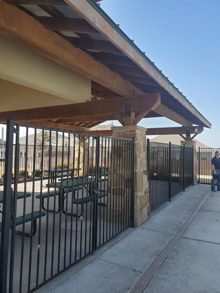 A man standing in front of a fence with picnic tables underneath it