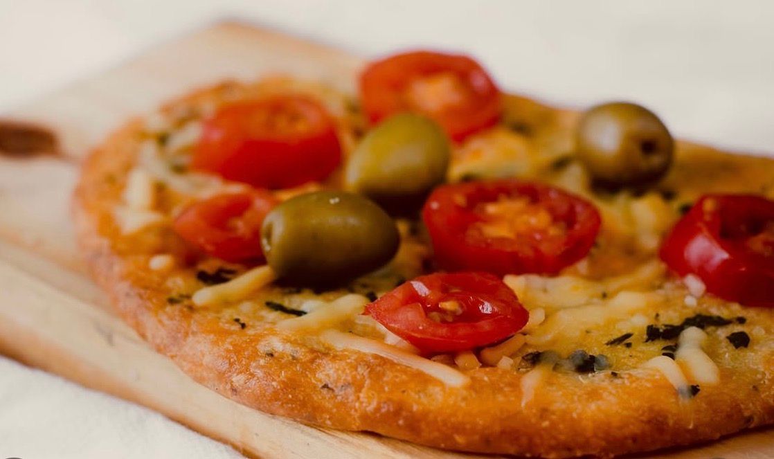 Pizza cubierta con tomates y aceitunas sobre una tabla de madera.